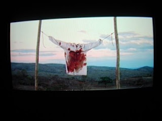 A bloodstained white shirt strung between two poles against a dusk sky, from Behind the Sun